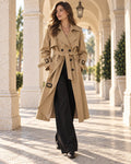 Woman wearing the City Trench Outfit: khaki double-breasted belted trench and black pleated wide-leg trousers
